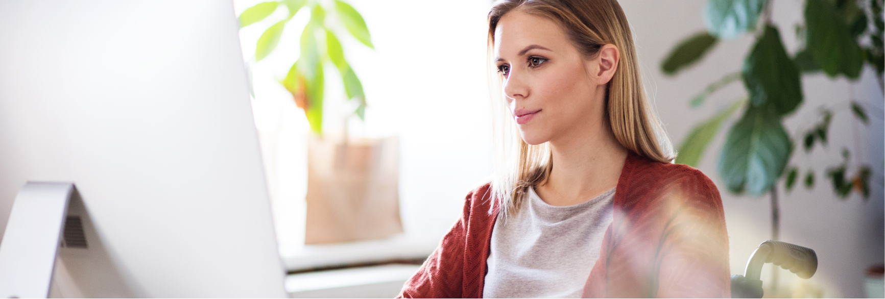 A photograph of a woman sitting in a wheelchair. She is looking pensively to the side. There are indoor plants in the background.
