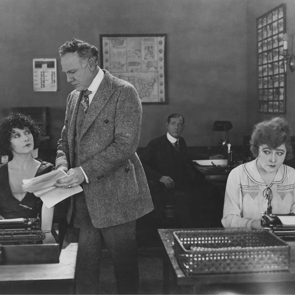 Manager talking with one secretary while another secretary looks on unhappily