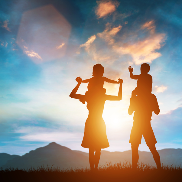 Two adults with their children in silhouette against a sunrise