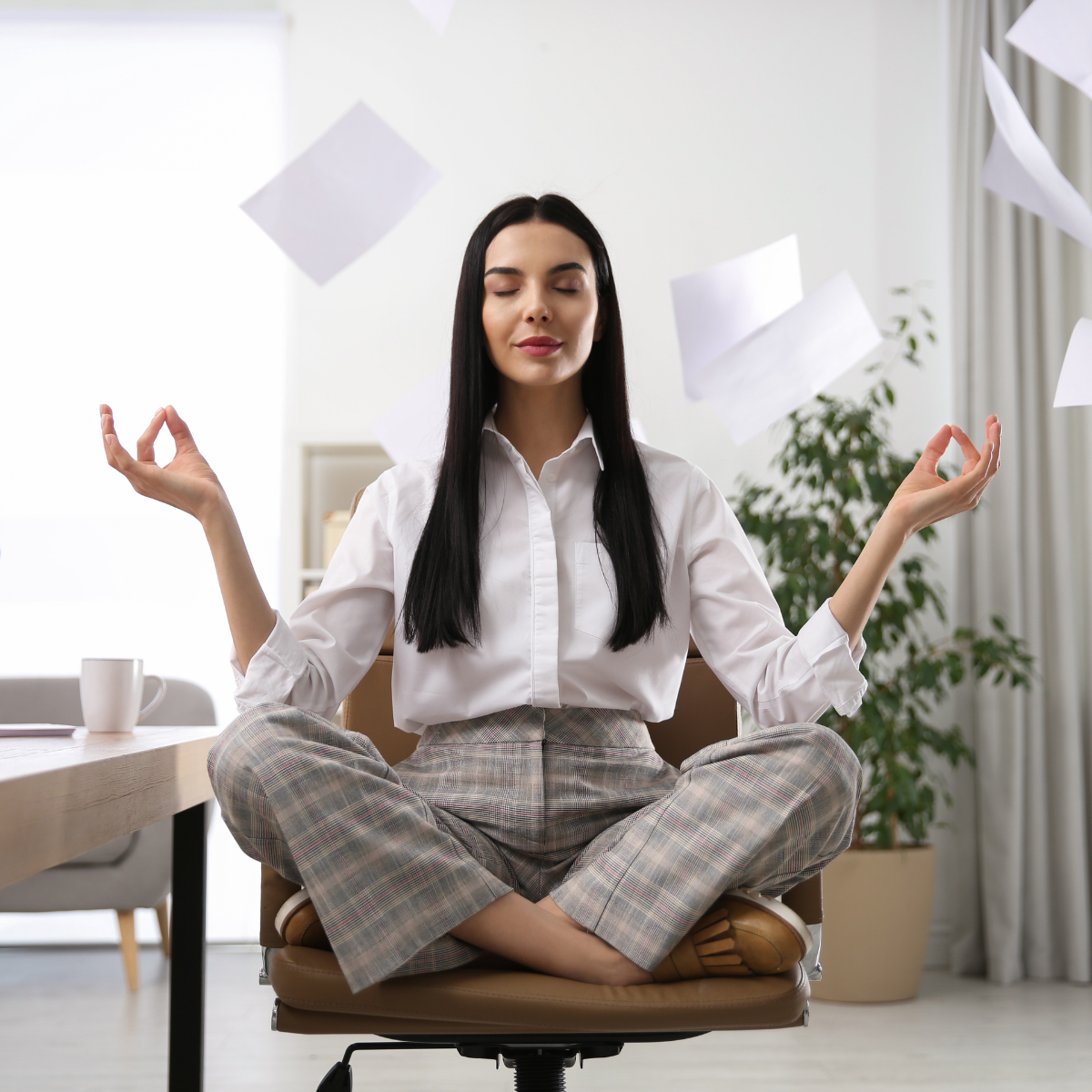 Girl seated in an office in a meditation pose with papers flying about her