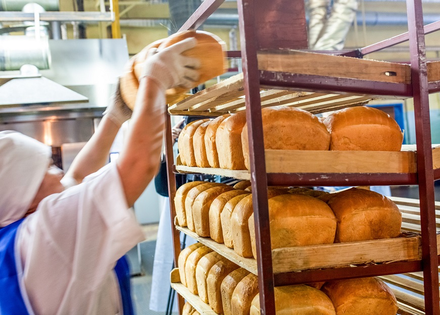 An image of a baker putting loaves of bread on shelves.